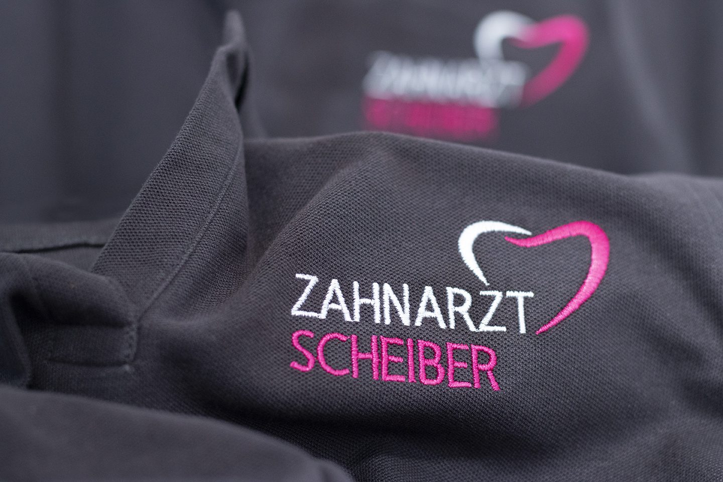Dunkles Polo mit weiß-pink gesticktem Logo Zahnarzt Scheiber
